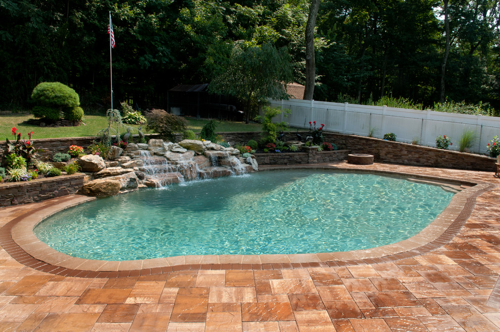 Imagen de piscina con fuente tradicional renovada de tamaño medio redondeada en patio trasero con adoquines de piedra natural