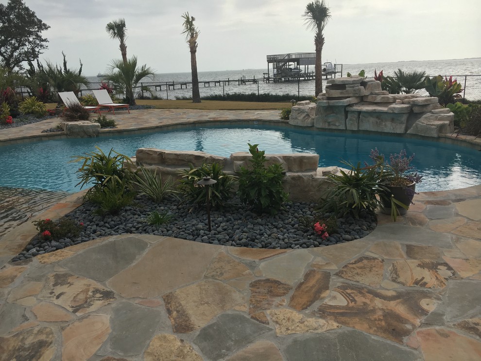 Foto de piscina con fuente alargada tropical de tamaño medio a medida en patio trasero con adoquines de piedra natural