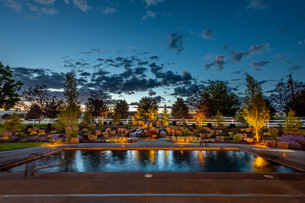 Foto de piscina alargada clásica renovada grande rectangular en patio trasero con paisajismo de piscina y losas de hormigón