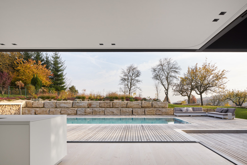 Cette photo montre un grand couloir de nage arrière moderne rectangle avec une terrasse en bois.