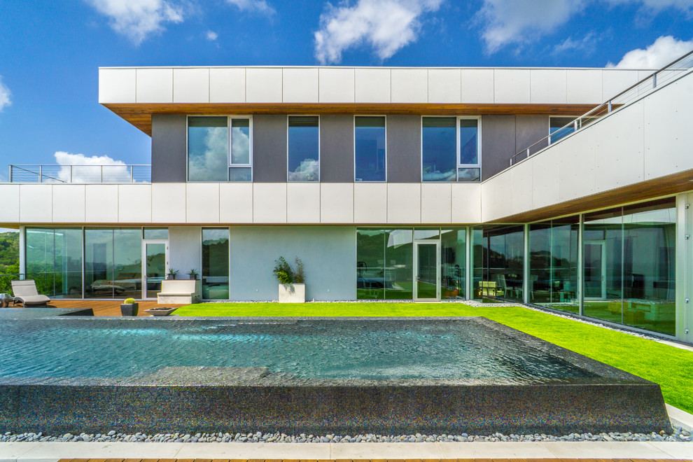 Réalisation d'une grande piscine à débordement minimaliste sur mesure avec un point d'eau, une cour et une terrasse en bois.