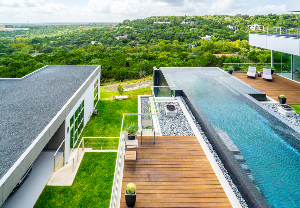 Cette image montre une grande piscine à débordement minimaliste sur mesure avec un point d'eau, une cour et une terrasse en bois.