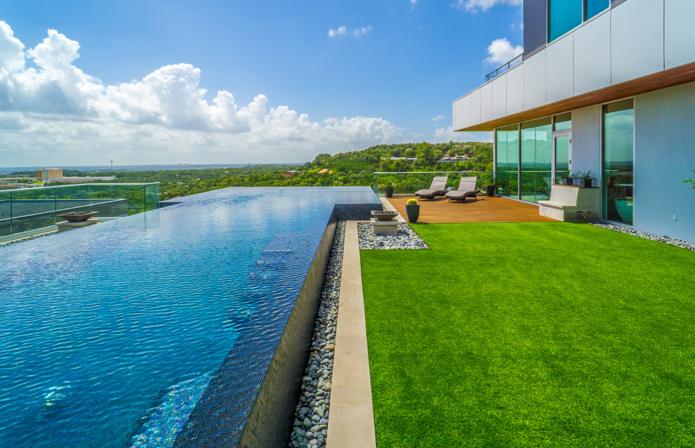 Photo of a large modern courtyard custom shaped infinity swimming pool in Austin with a water feature and decking.