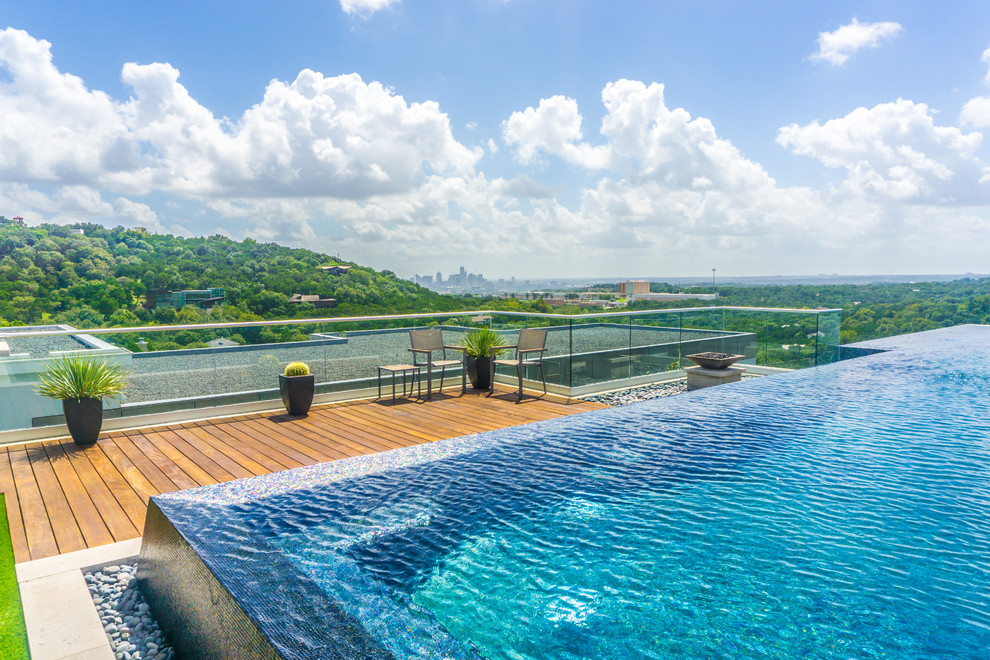 Cette photo montre une grande piscine à débordement moderne sur mesure avec un point d'eau, une cour et une terrasse en bois.
