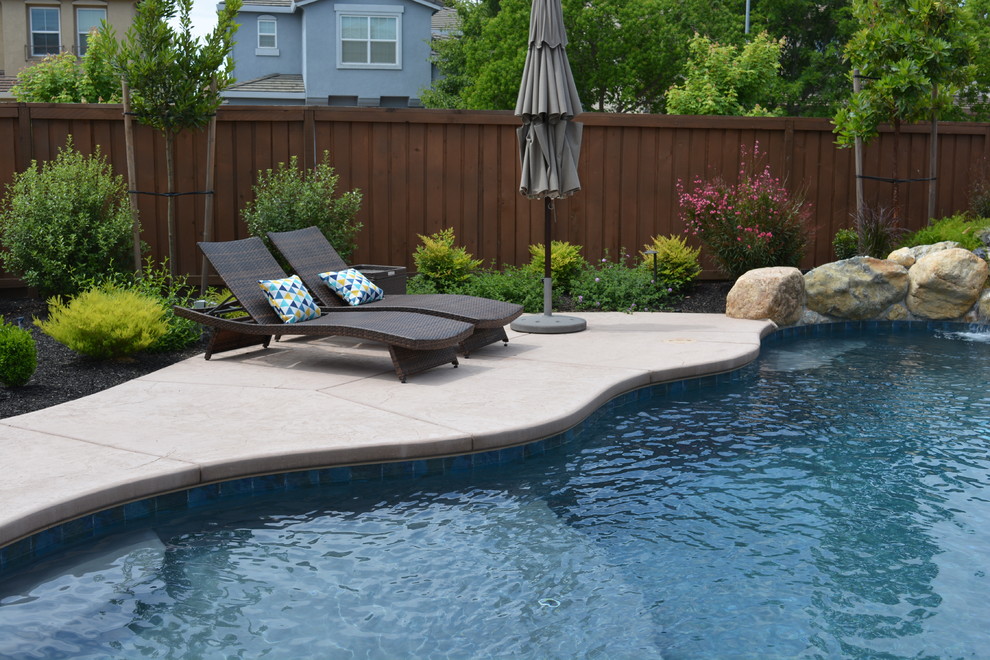 Photo of a medium sized shabby-chic style back custom shaped natural swimming pool in Sacramento with a water feature and natural stone paving.