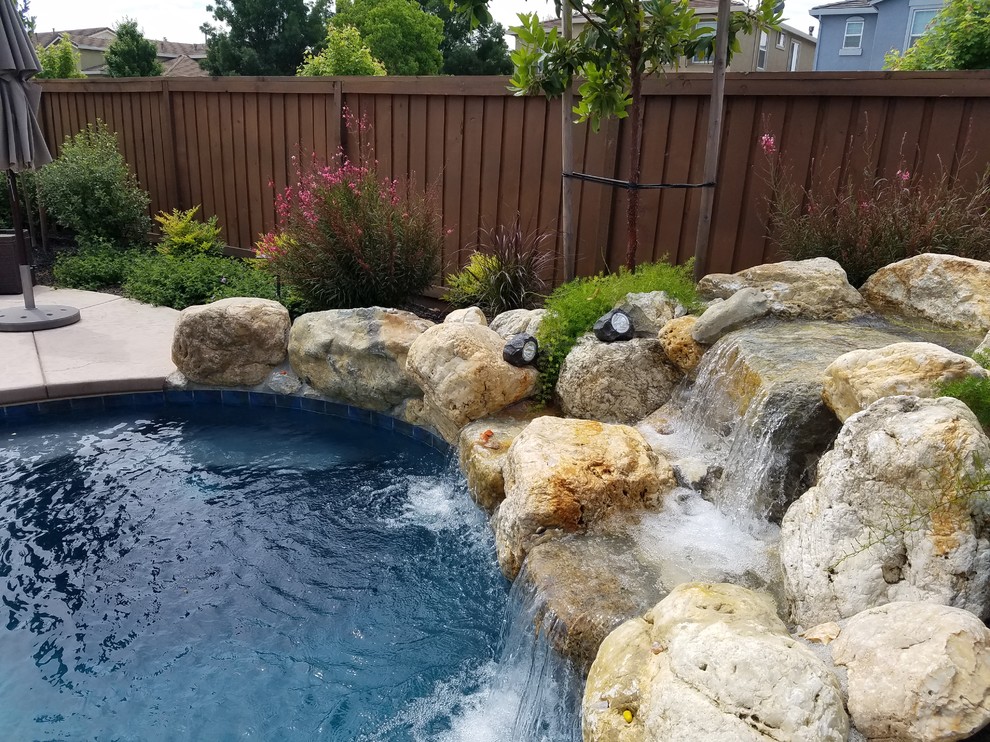 Medium sized vintage back custom shaped natural swimming pool in Sacramento with a water feature and natural stone paving.