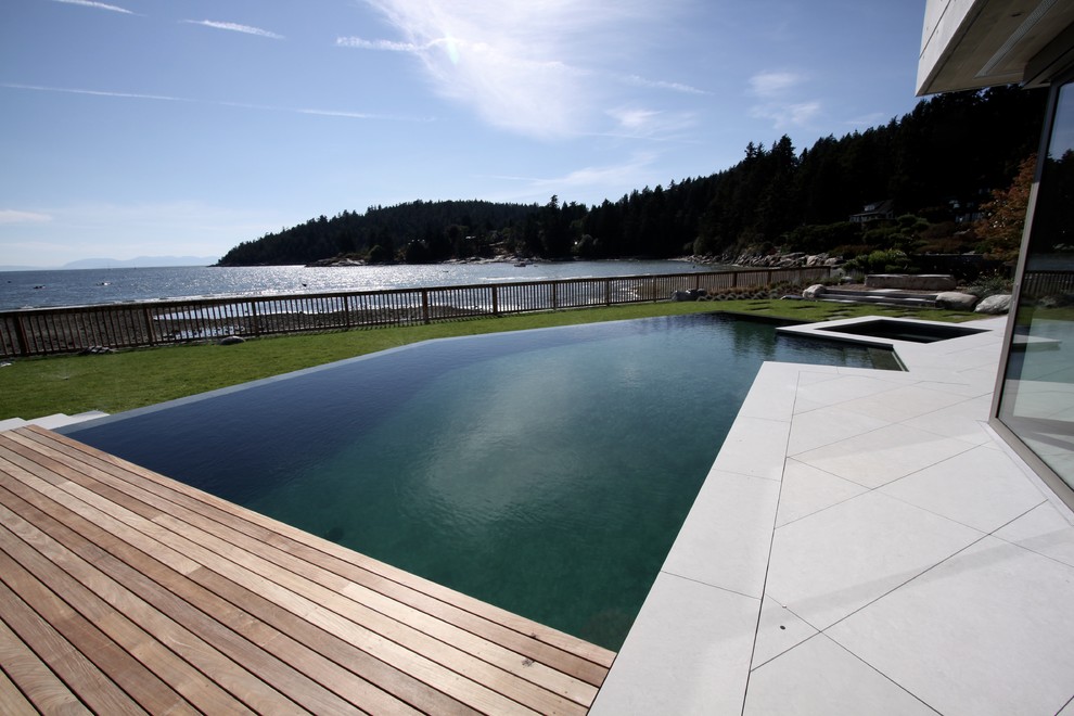 Idée de décoration pour une grande piscine à débordement et arrière minimaliste sur mesure avec un bain bouillonnant et des pavés en pierre naturelle.