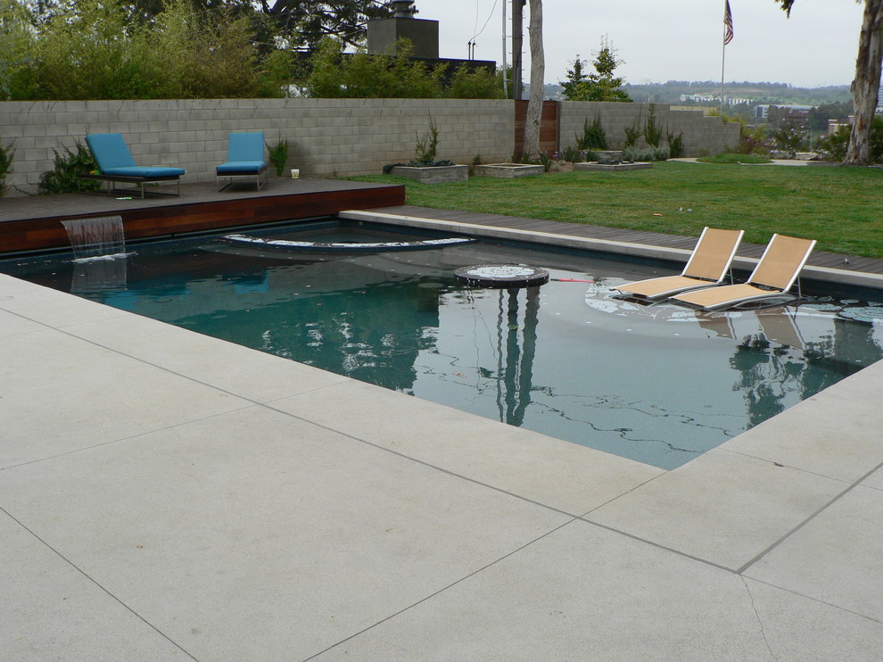 Cette image montre un grand couloir de nage arrière design rectangle avec une dalle de béton et un bain bouillonnant.