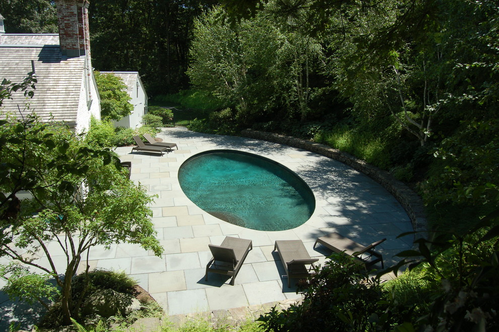 Foto de piscina clásica de tamaño medio redondeada en patio trasero con adoquines de piedra natural