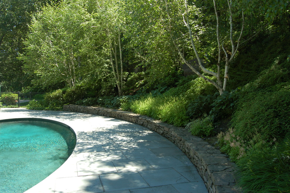 Klassisk inredning av en mellanstor rund pool på baksidan av huset, med naturstensplattor