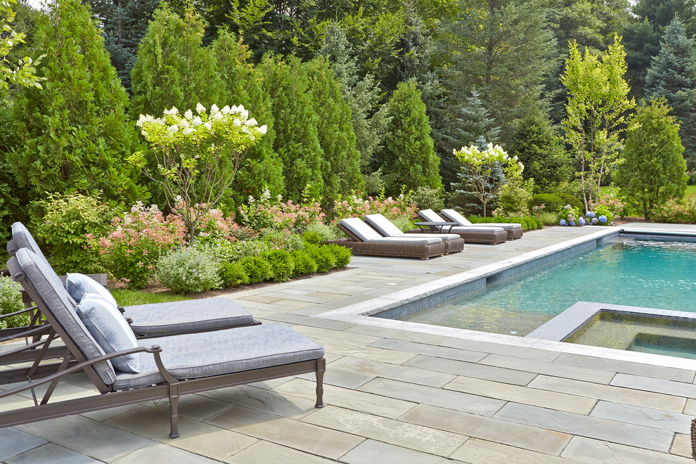 Cette image montre une grande piscine naturelle et arrière traditionnelle rectangle avec un bain bouillonnant et des pavés en pierre naturelle.