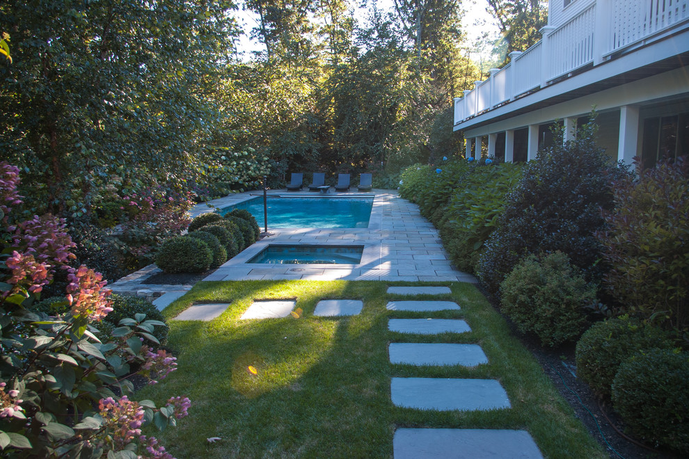 Cette image montre une grande piscine arrière traditionnelle rectangle avec un bain bouillonnant et des pavés en pierre naturelle.