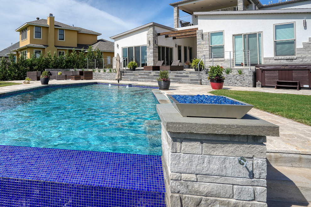 Diseño de piscina infinita contemporánea de tamaño medio en forma de L en patio trasero con adoquines de piedra natural