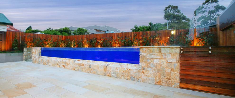 Large contemporary back rectangular above ground swimming pool in Melbourne with natural stone paving.