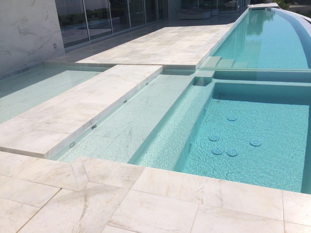 Foto de piscina infinita moderna extra grande en forma de L en patio trasero con suelo de baldosas