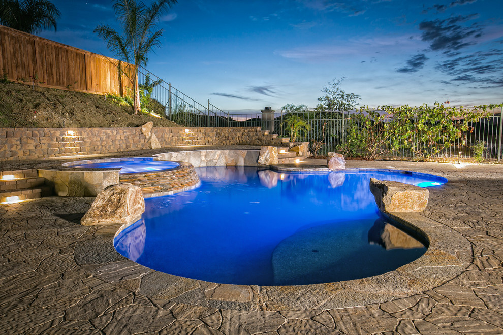 На фото: огромный естественный бассейн произвольной формы на заднем дворе в стиле рустика с джакузи и мощением тротуарной плиткой с