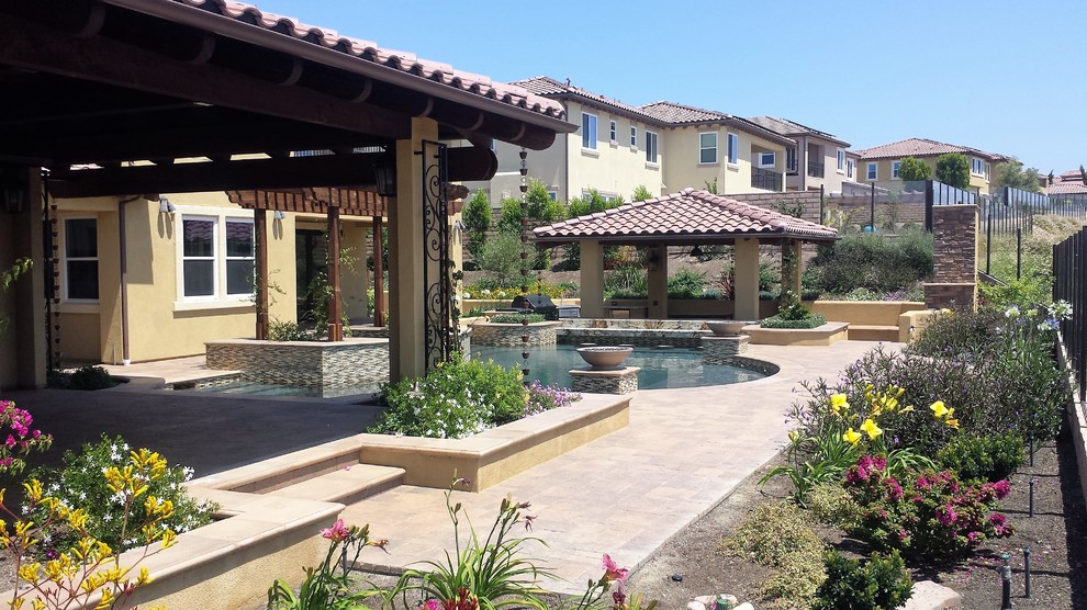 Large tuscan backyard concrete paver and custom-shaped hot tub photo in San Diego