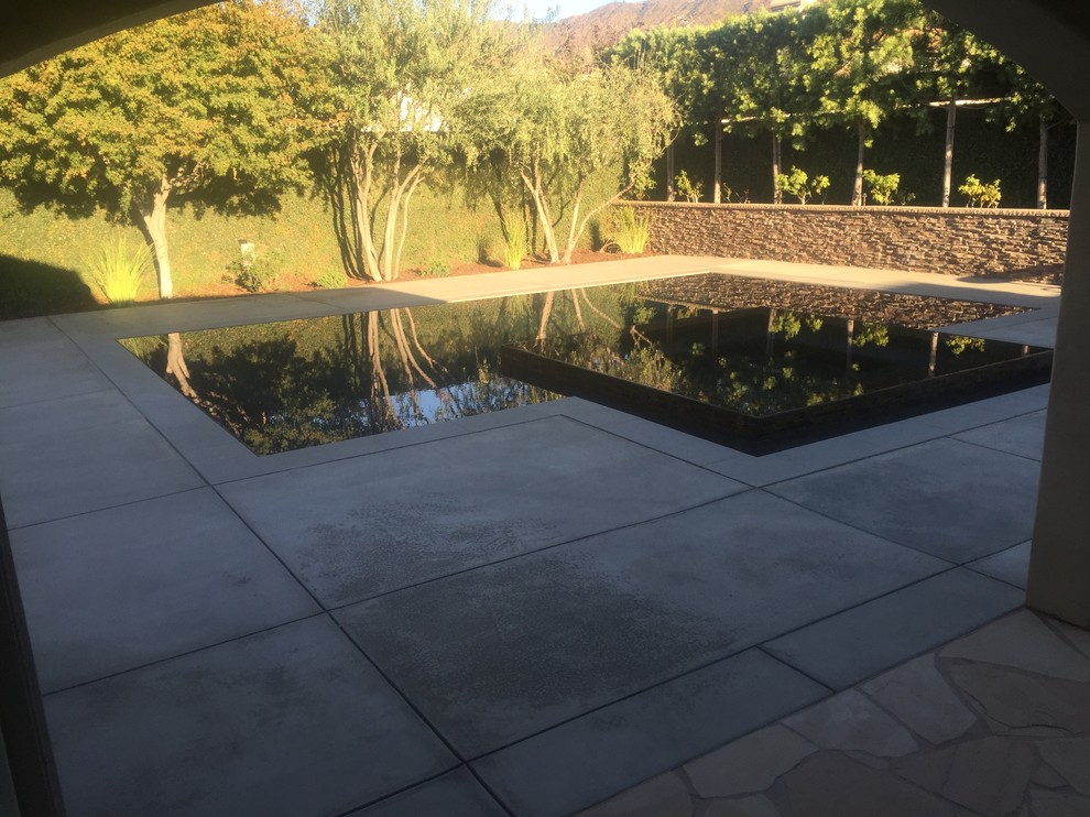 This is an example of a medium sized modern back l-shaped infinity hot tub in Los Angeles with concrete paving.