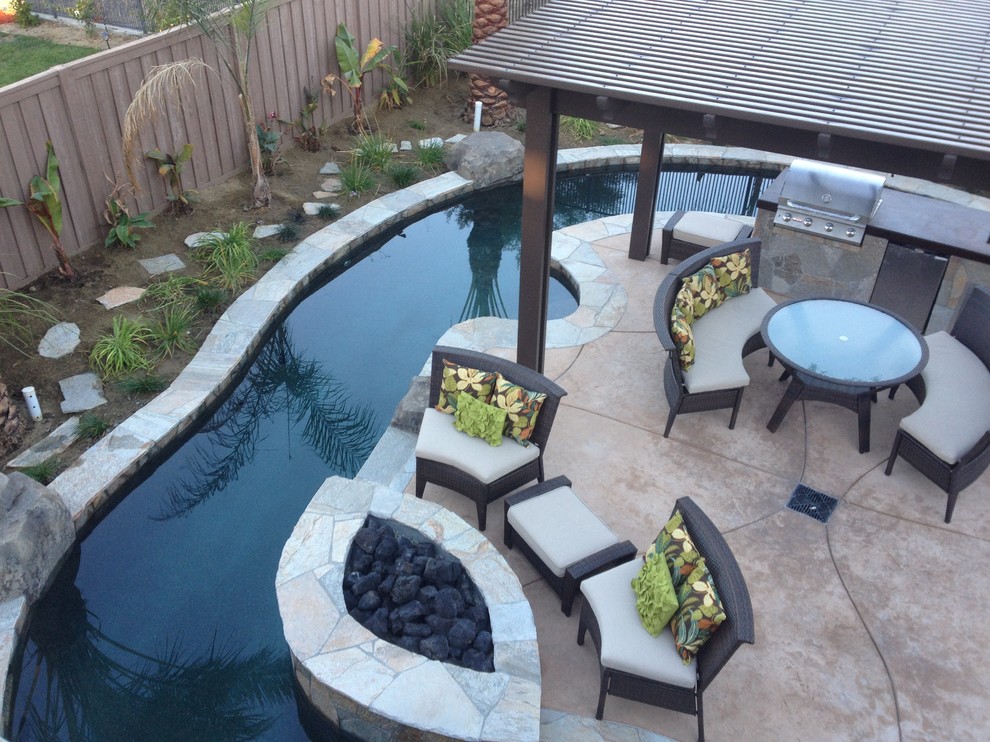 Ispirazione per una grande piscina naturale tropicale personalizzata dietro casa con fontane e lastre di cemento
