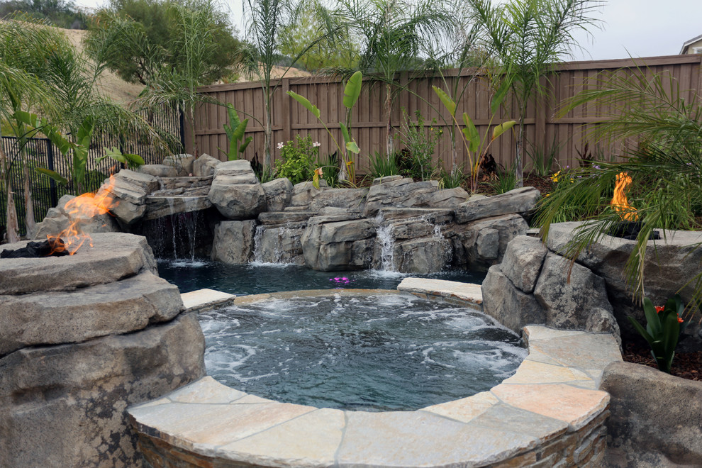 Idee per una grande piscina naturale tropicale personalizzata dietro casa con fontane e lastre di cemento