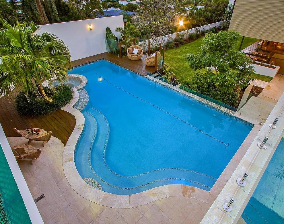 Ispirazione per una piscina a sfioro infinito tropicale personalizzata di medie dimensioni e dietro casa con una dépendance a bordo piscina e pavimentazioni in pietra naturale