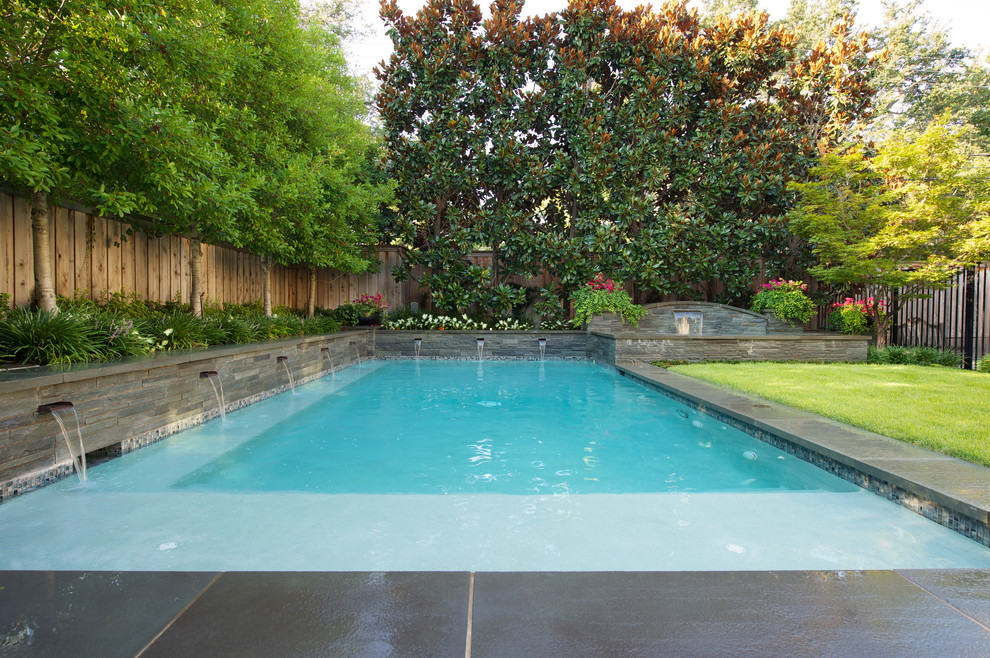 Large traditional back rectangular infinity swimming pool in Dallas with a water feature and natural stone paving.