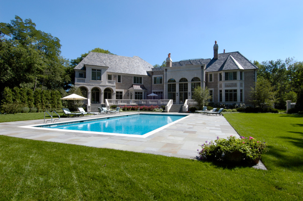Diseño de piscina alargada tradicional grande rectangular en patio trasero con adoquines de piedra natural