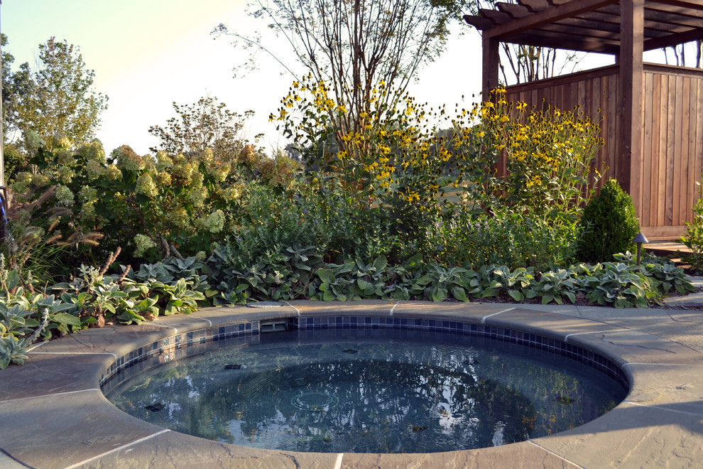 Hot tub - mid-sized contemporary backyard stone and round infinity hot tub idea in Other
