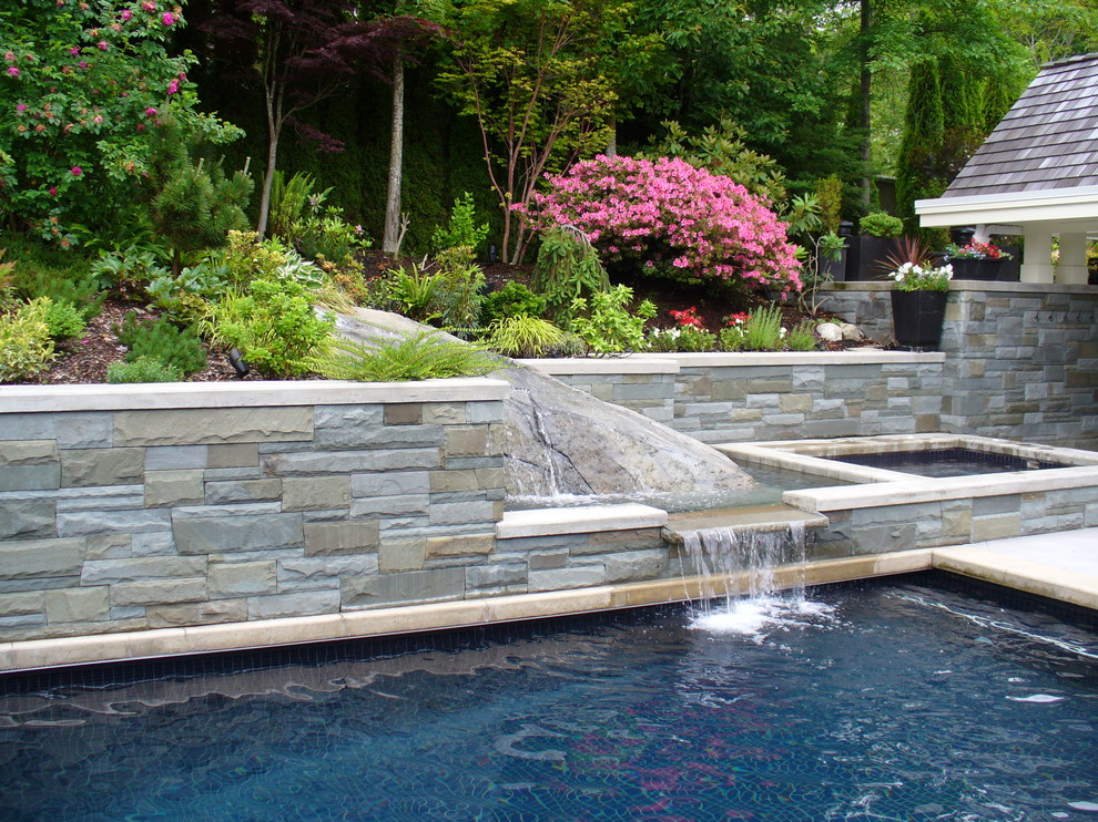 Modelo de piscina con fuente alargada actual de tamaño medio rectangular en patio trasero con adoquines de hormigón