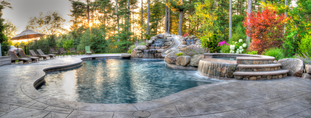Ejemplo de piscina con tobogán alargada rural grande a medida en patio trasero con suelo de hormigón estampado