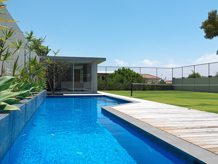 Пример оригинального дизайна: большой спортивный, угловой бассейн на заднем дворе в современном стиле с домиком у бассейна и покрытием из каменной брусчатки