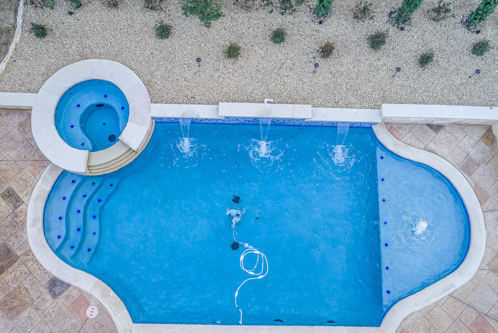This is an example of a medium sized mediterranean back custom shaped natural swimming pool in Dallas with a water feature and stamped concrete.