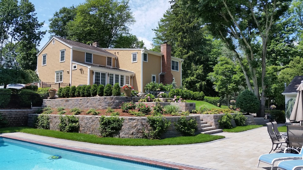 Ejemplo de piscina alargada clásica grande a medida en patio trasero con adoquines de piedra natural