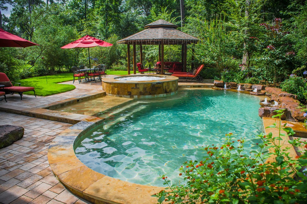 Aménagement d'une piscine arrière classique de taille moyenne et sur mesure avec un bain bouillonnant et des pavés en pierre naturelle.