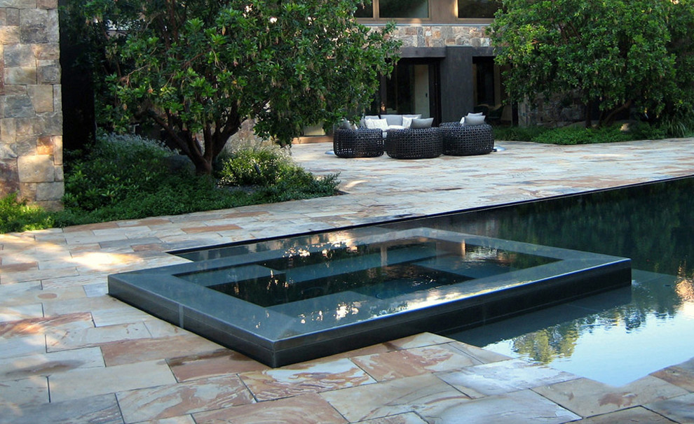 Cette image montre une piscine à débordement et arrière bohème de taille moyenne avec des pavés en pierre naturelle.