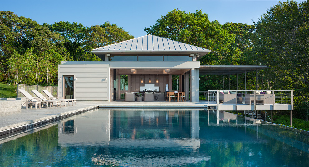 На фото: большой прямоугольный бассейн на заднем дворе в современном стиле с домиком у бассейна и покрытием из бетонных плит