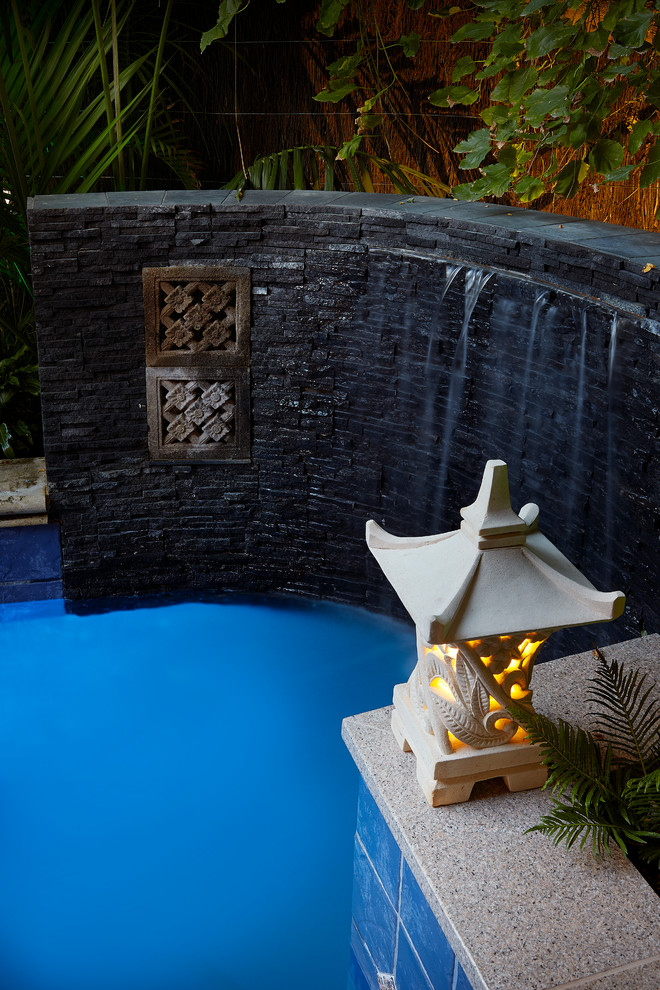 Aménagement d'une petite piscine arrière exotique sur mesure avec un point d'eau et une terrasse en bois.