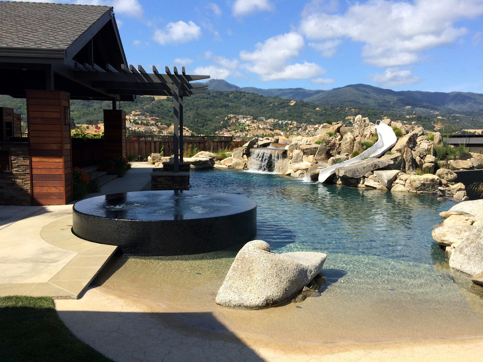 Diseño de piscina con tobogán infinita actual extra grande a medida en patio trasero con adoquines de piedra natural