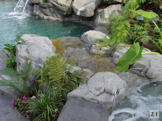 Esempio di una grande piscina naturale stile americano personalizzata dietro casa con fontane e lastre di cemento