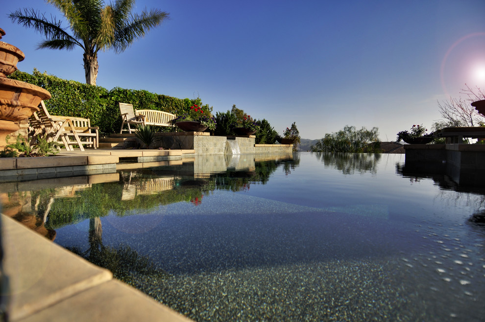 Photo of a large mediterranean back custom shaped infinity swimming pool in Orange County with concrete slabs.