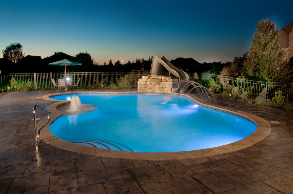 Immagine di una piscina chic personalizzata di medie dimensioni e dietro casa con un acquascivolo e pavimentazioni in cemento