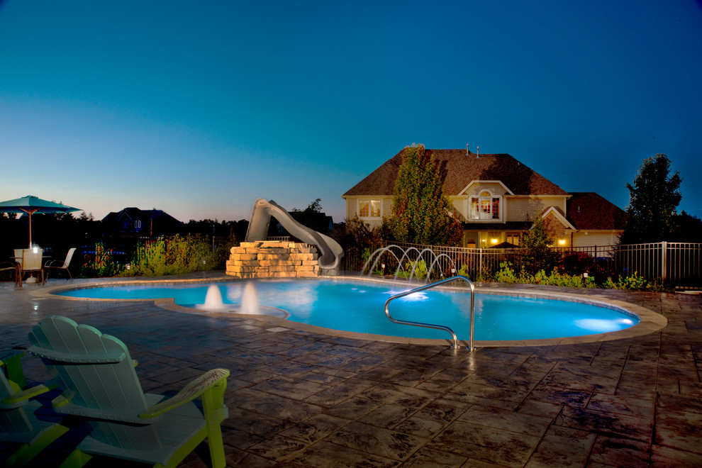 Diseño de piscina con tobogán clásica de tamaño medio a medida en patio trasero con adoquines de hormigón
