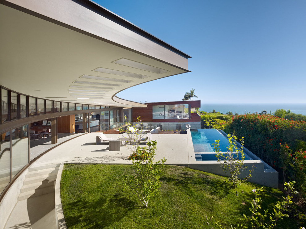 Diseño de piscinas y jacuzzis infinitos actuales extra grandes rectangulares en patio trasero con losas de hormigón