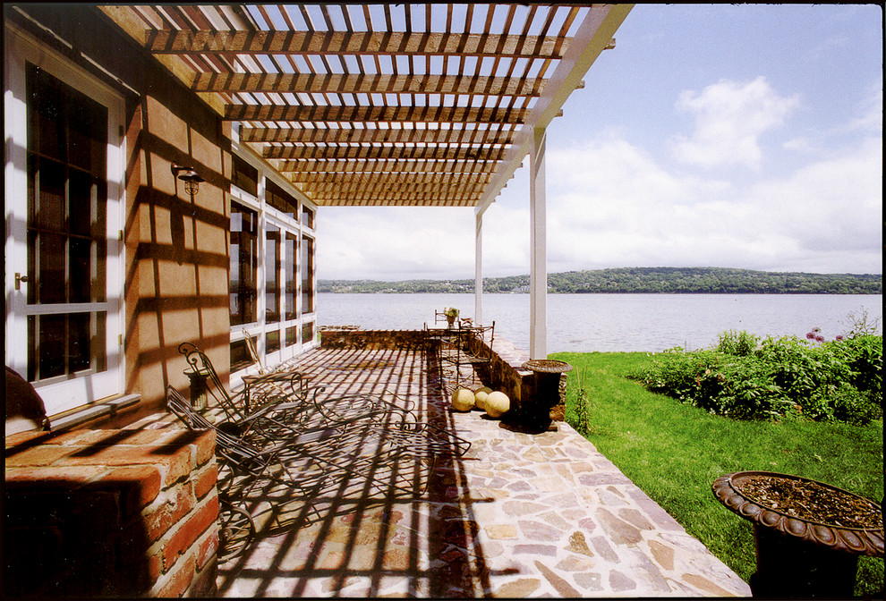 Imagen de terraza de estilo de casa de campo de tamaño medio en patio trasero con adoquines de piedra natural y pérgola