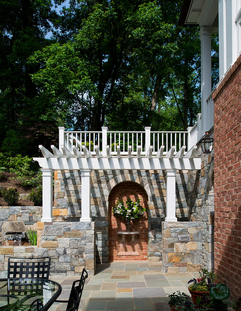 Cette image montre un grand porche d'entrée de maison arrière traditionnel avec des pavés en pierre naturelle et une pergola.