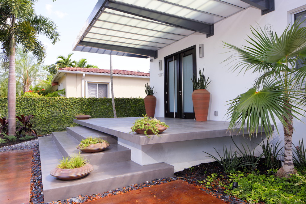 Photo of a medium sized modern front veranda in Miami with concrete slabs and an awning.
