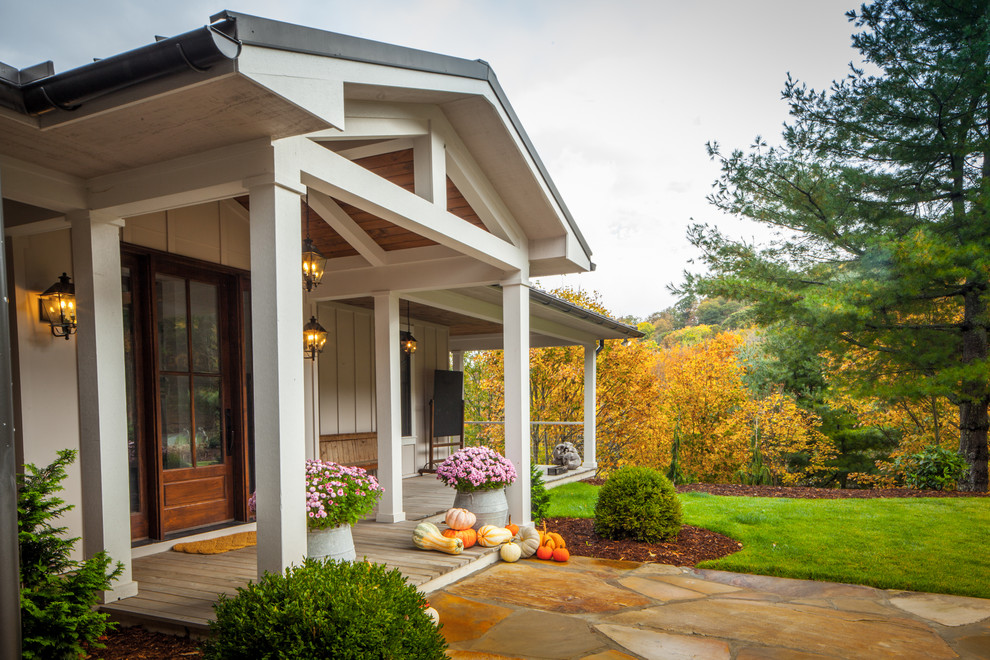 Cette image montre un grand porche d'entrée de maison arrière rustique avec une terrasse en bois et une extension de toiture.