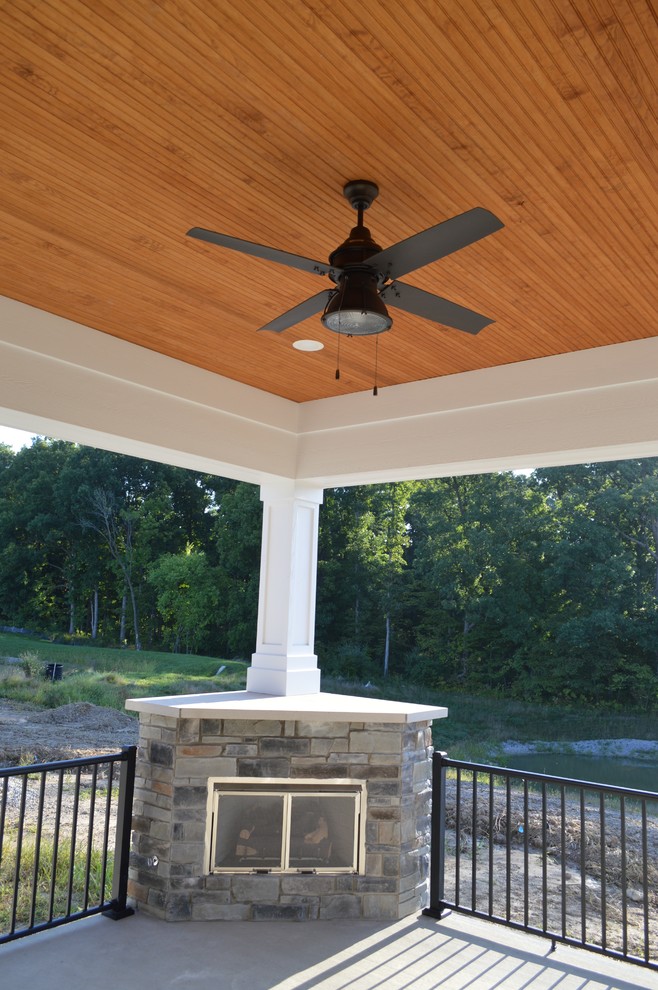 Idée de décoration pour un grand porche d'entrée de maison arrière craftsman avec une cheminée, une dalle de béton et une extension de toiture.