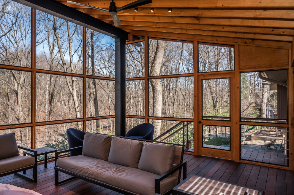 This is an example of a mid-sized modern stone screened-in back porch design in DC Metro with a roof extension.