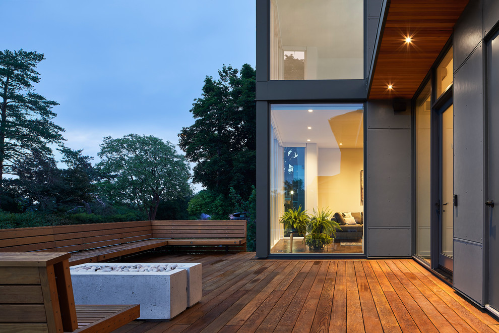 Cette photo montre un grand porche d'entrée de maison arrière moderne avec un foyer extérieur et une terrasse en bois.